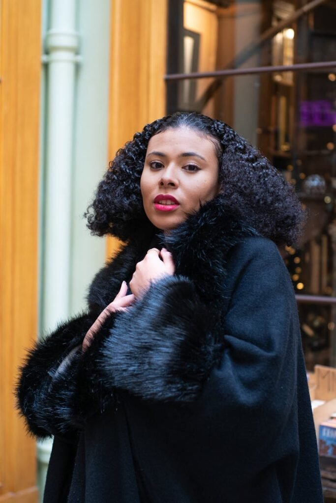Fashionable woman posing in a cozy Paris bookstore with festive decorations and black fur coat.